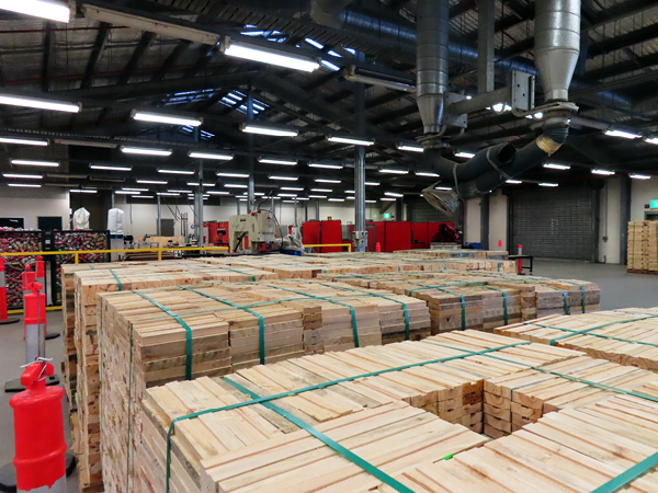 A large warehouse space with pallets of wood in foreground, in the background are large containers of empty drink containers to be recycled and industrial equipment.